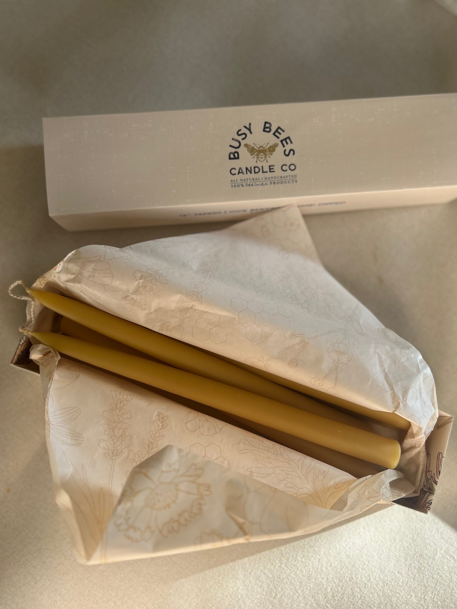 Busy Bees Hand Dipped 12 Inch Taper Candles wrapped in branded paper packaging on a neutral fabric background.