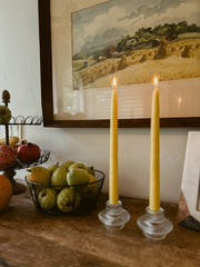 Busy Bees taper candles from The Queen Bee Bundle displayed on brass candle holders beside fruit and framed artwork.