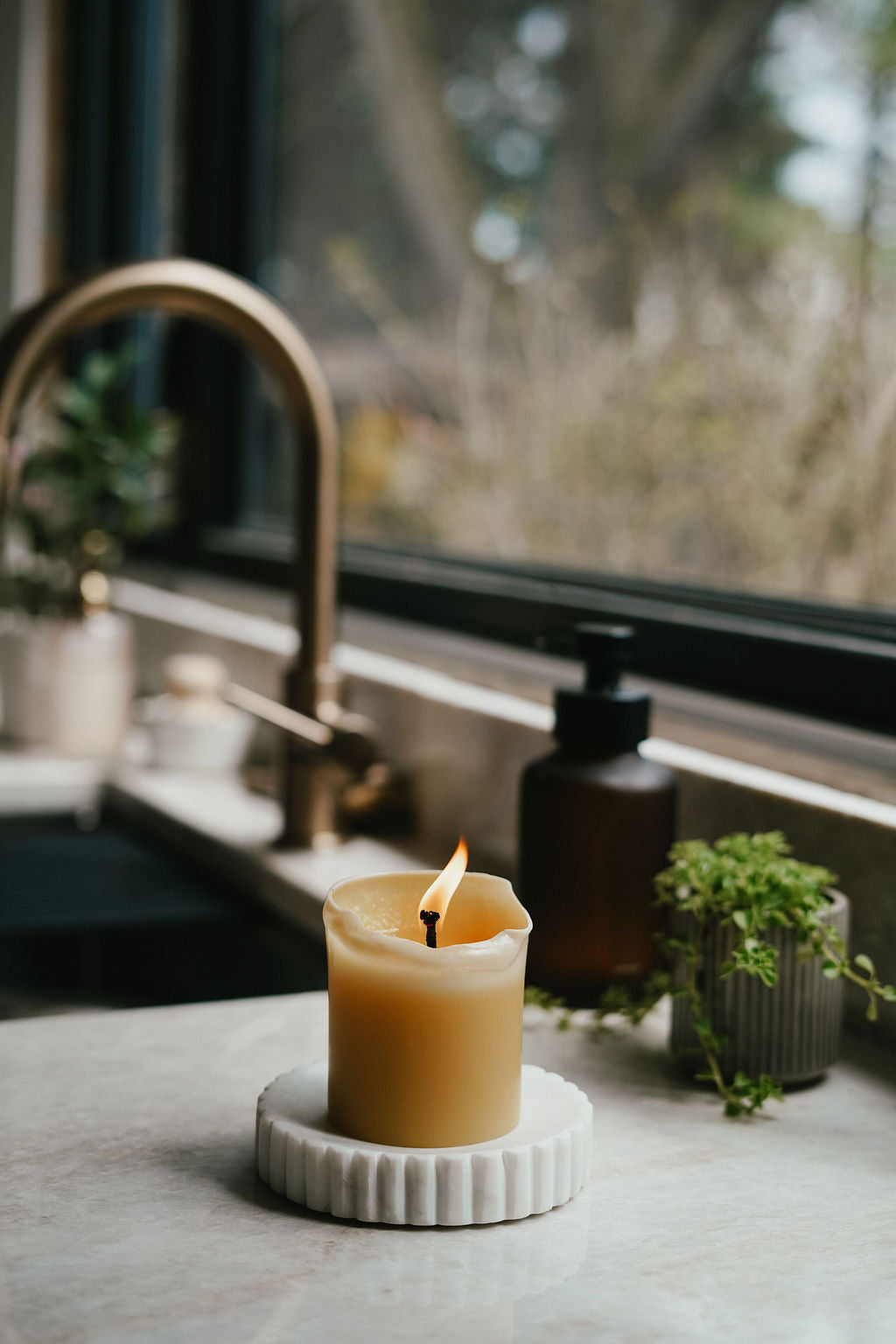 Busy Bees 3 Inch by 3.5 Inch pillar candle burning beside a kitchen sink with natural light coming through the window.