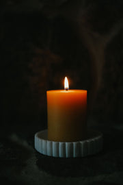 Lit Busy Bees 3 Inch by 3.5 Inch pillar candle glowing in a dark setting on a ribbed ceramic holder.