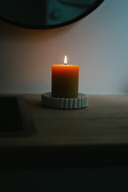 Busy Bees 3 Inch by 3.5 Inch pillar candle burning on a ceramic tray in a softly lit room.