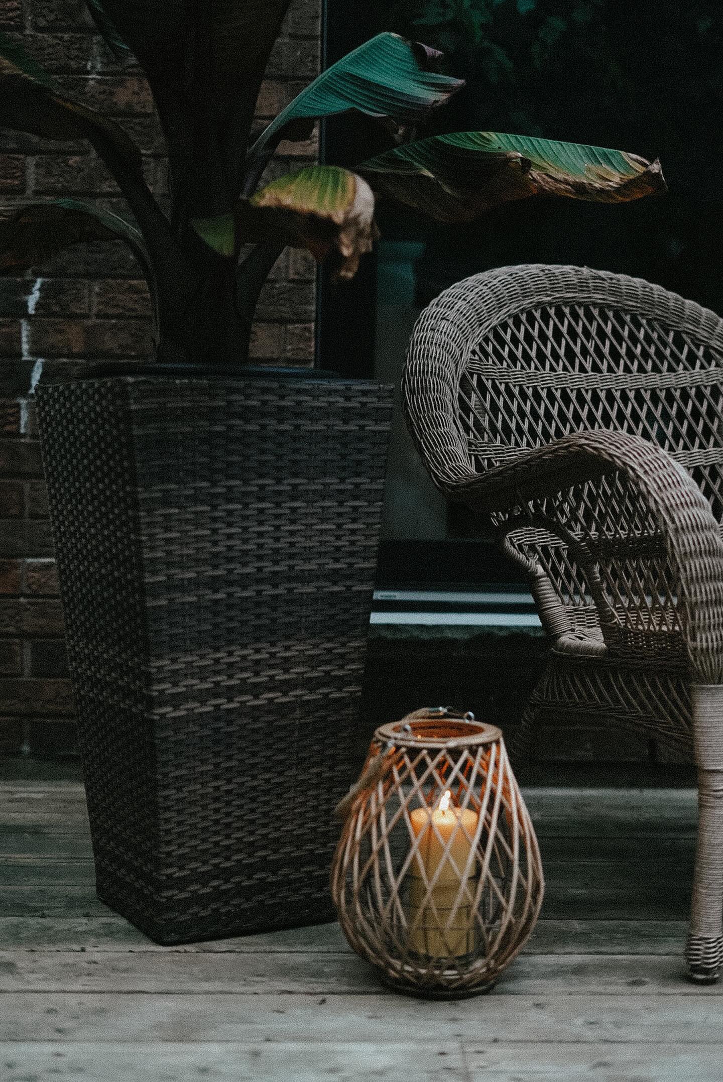 Lit Busy Bees 3 Inch by 6 Inch pillar candle glowing beside a dark ribbed glass holder on a windowsill.