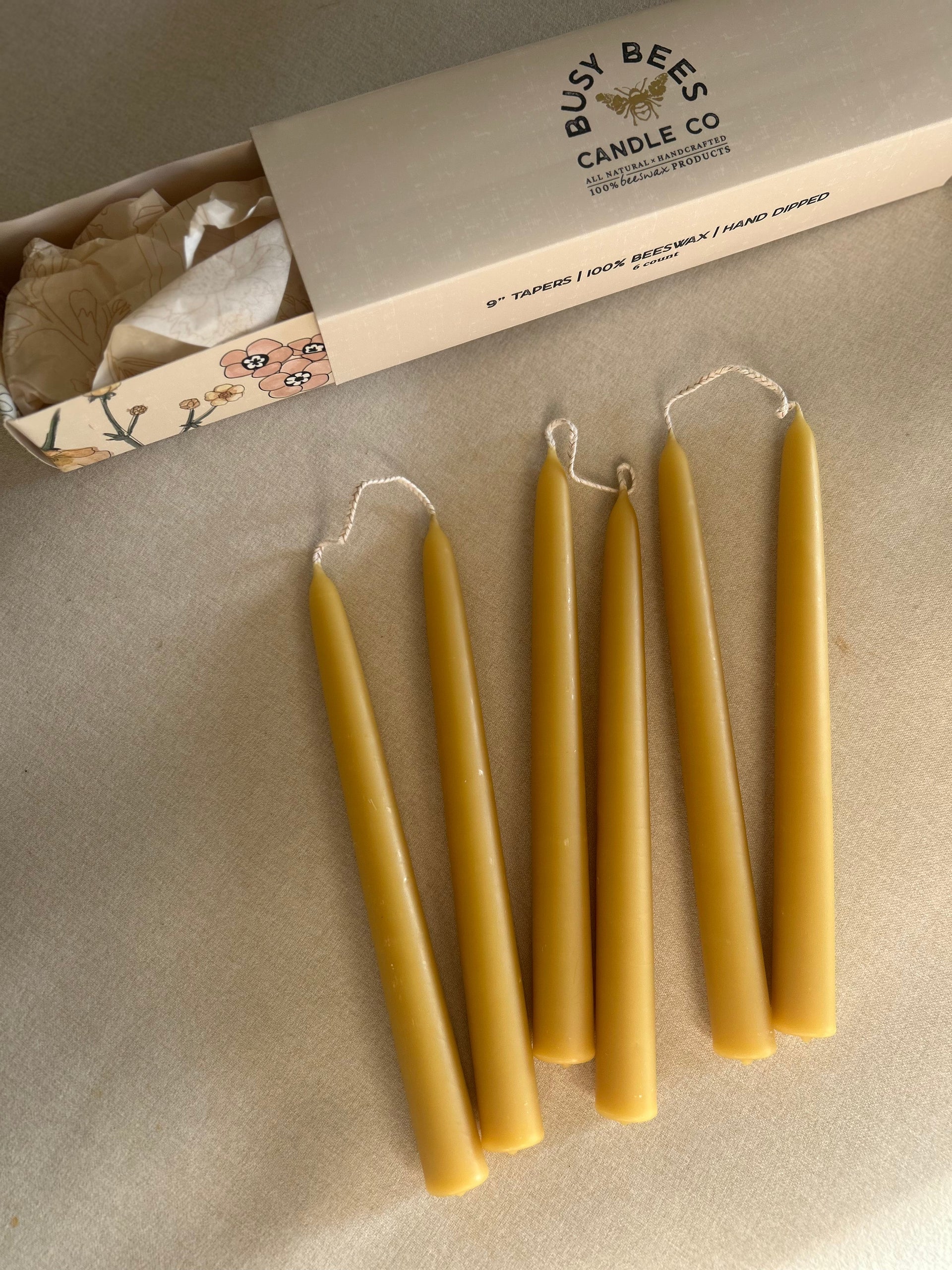 Busy Bees Hand Dipped 9 Inch Taper Candles 6 Pack arranged beside branded packaging on a soft neutral surface.