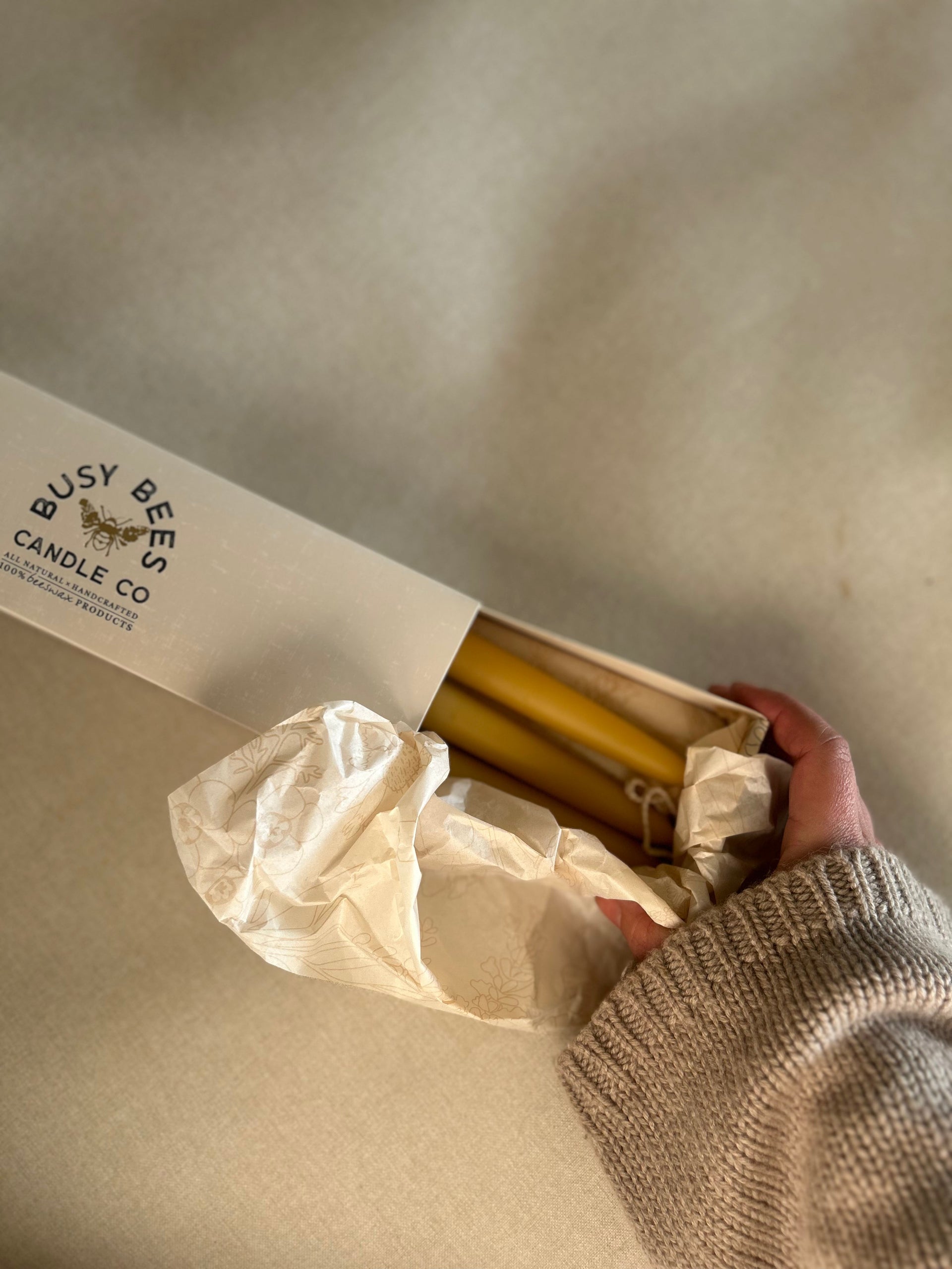Close up of Busy Bees Hand Dipped 9 Inch Taper Candles 6 Pack being removed from branded packaging in soft natural light.
