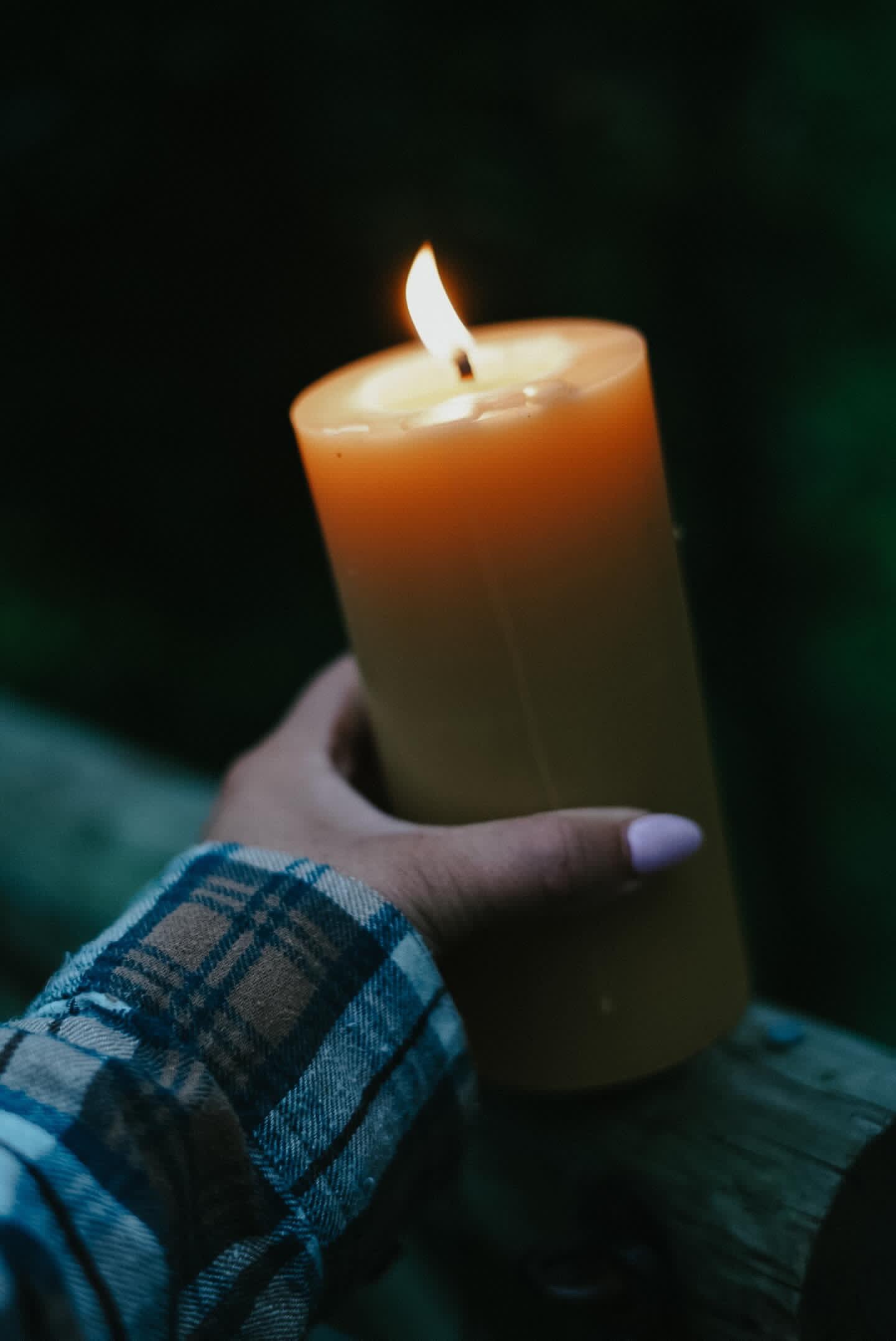 Person holding a lit Busy Bees pillar candle from The Queen Bee Bundle outdoors at dusk.