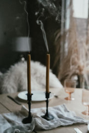 Lit Busy Bees Hand Dipped 9 Inch Taper Candles displayed beside glassware in a moody indoor setting.