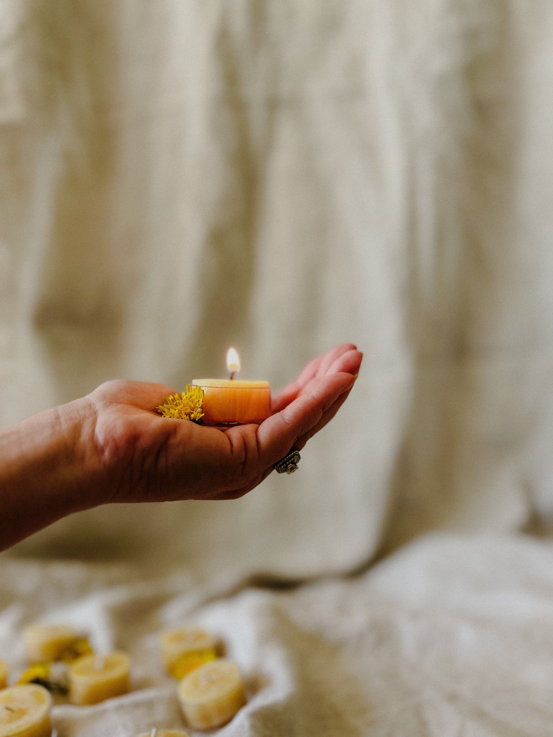 Hand holding a single Busy Bees Bulk Loose Tea Light Candle above draped neutral fabric.