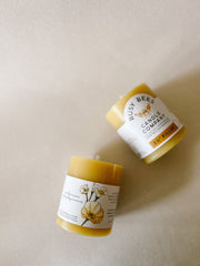 Two Busy Bees 3 Inch by 3.5 Inch pillar candles with branded labels arranged on neutral fabric.