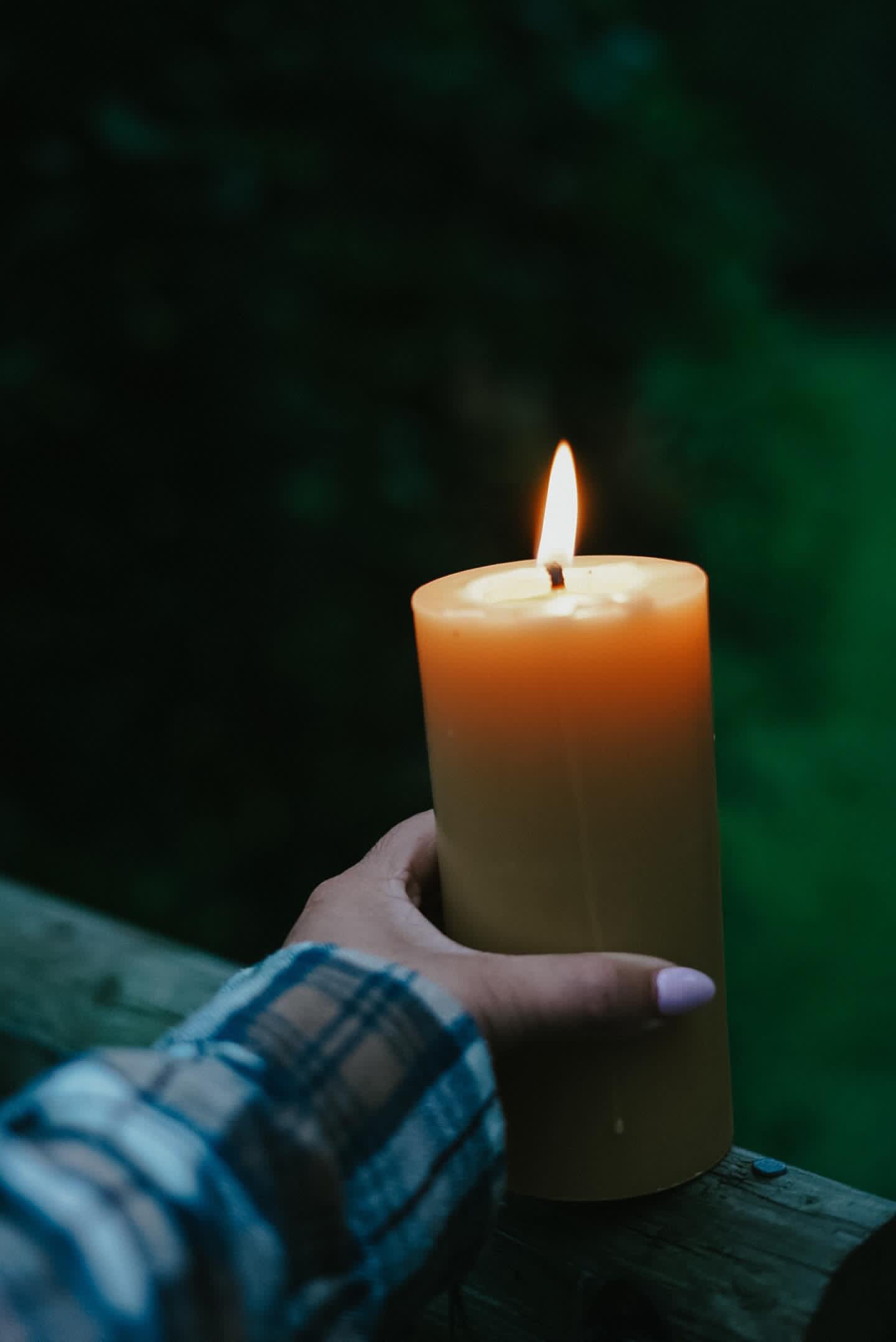 Lit Busy Bees 3 Inch by 6 Inch pillar candle displayed outdoors at dusk with soft shadows and greenery in the background.
