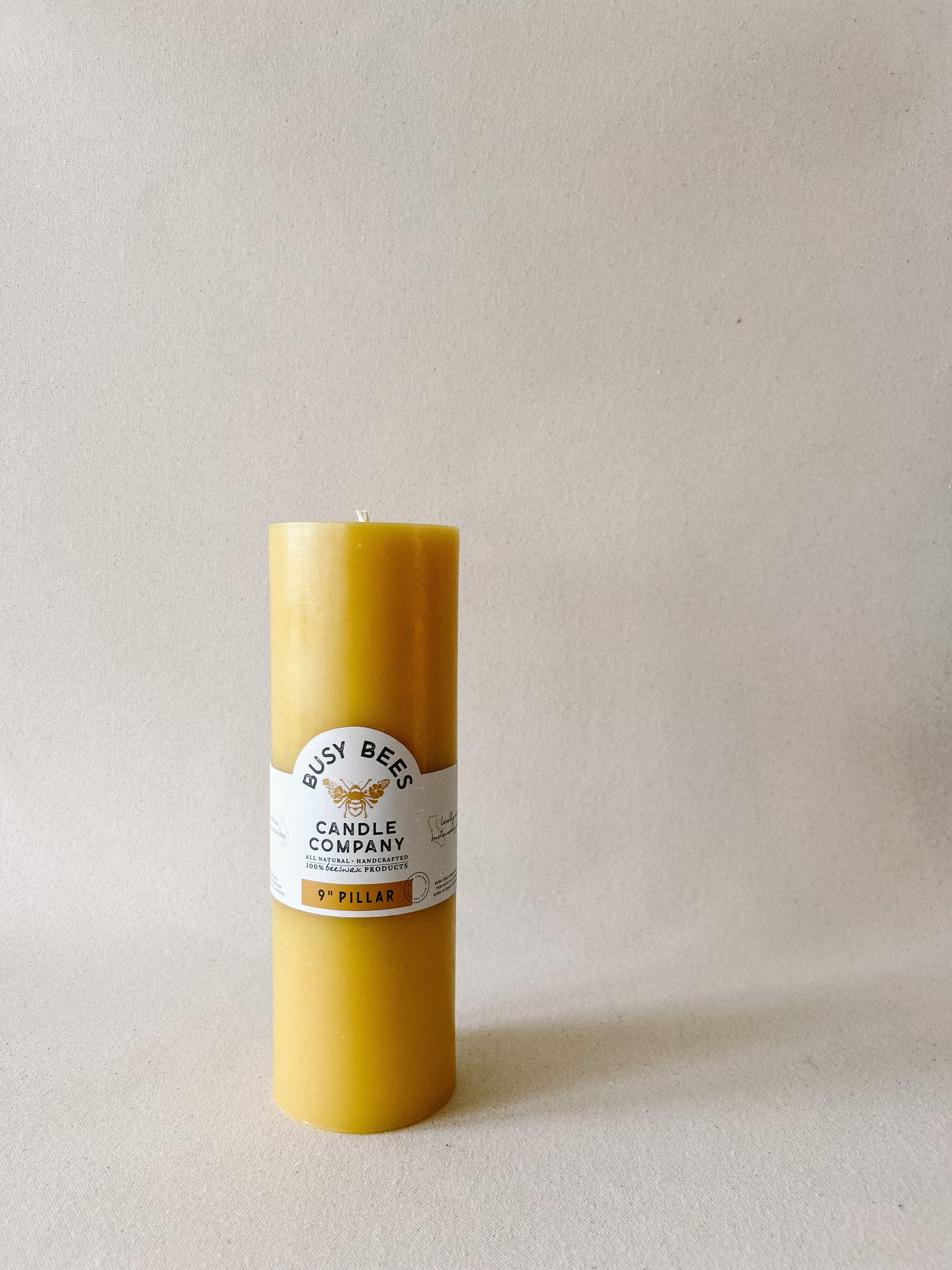 Busy Bees 3 Inch Pillar Trio beeswax candle with branded label displayed in soft natural lighting.