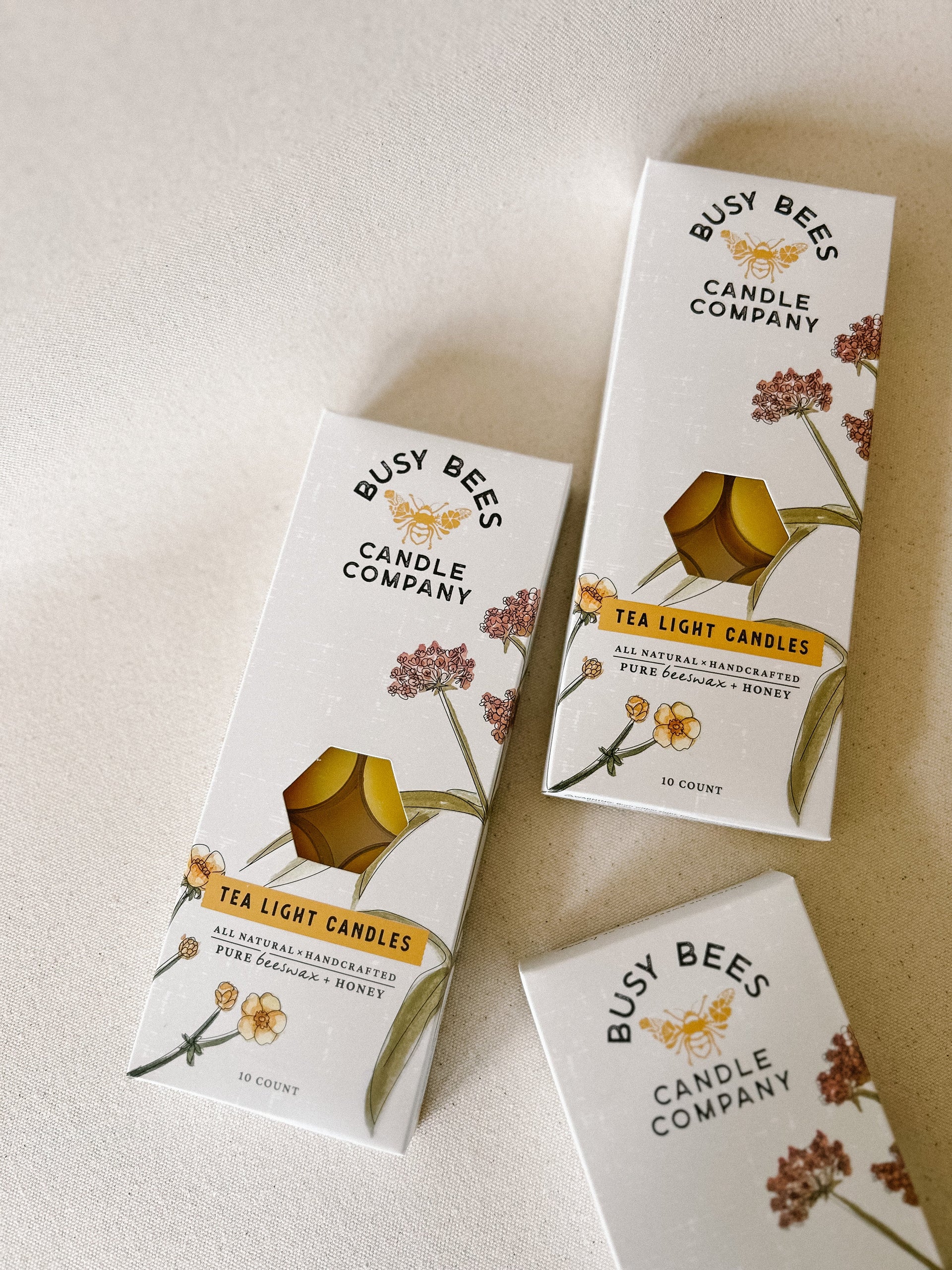 Stacked Busy Bees Tea Light Candles Box 10ct packaging displayed on a soft neutral surface with branded bee illustrations visible.