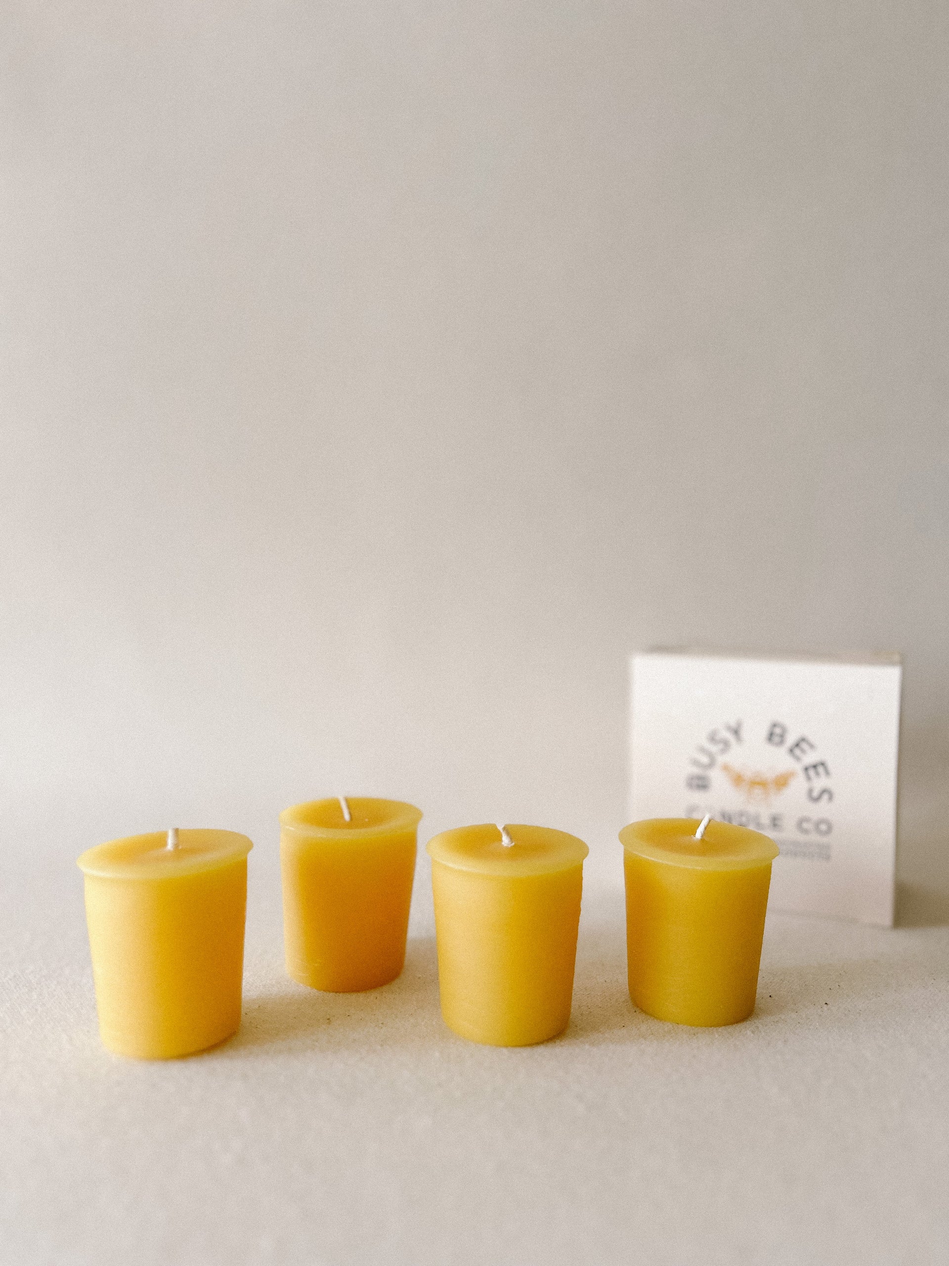 Busy Bees Votive Candles 4 Pack arranged on a soft neutral surface beside branded packaging.
