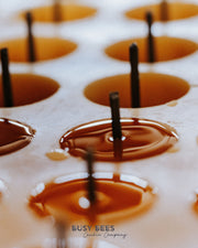Close up of lit Busy Bees tea lights from The Queen Bee Bundle with warm reflections across melted wax.
