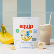 Equip Kids Banana Split Protein Powder pouch with bananas, a smoothie, and a scoop of powder on a blue tiled backdrop.