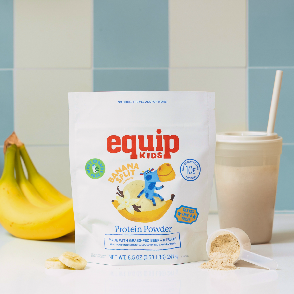 Equip Kids Banana Split Protein Powder pouch with bananas, a smoothie, and a scoop of powder on a blue tiled backdrop.