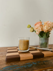 Busy Bees Classic Beeswax Jar Candle 12oz styled beside flowers and stacked books on a cozy wooden table.