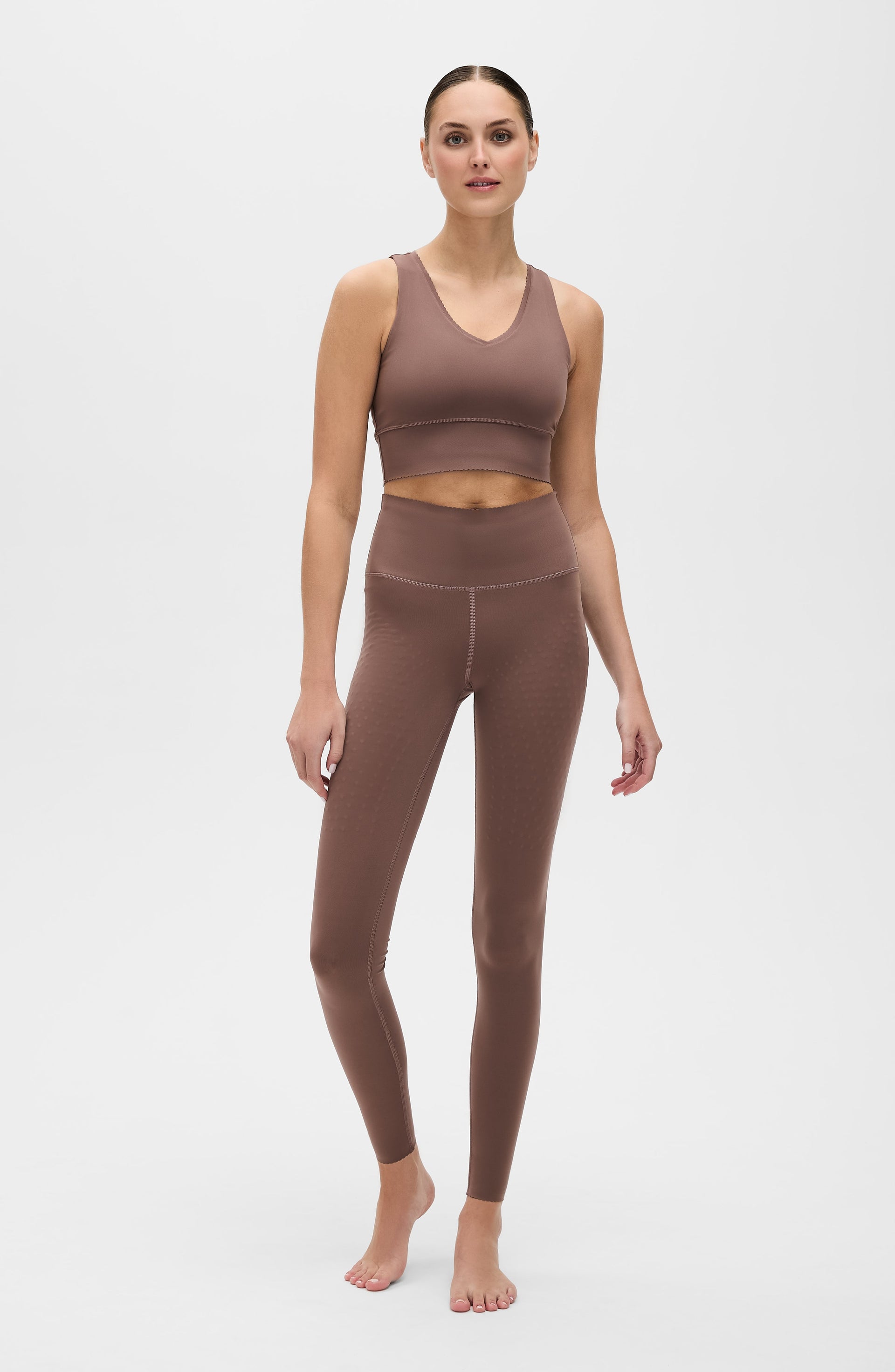 Full body portrait of a woman wearing the Elastique Athletics Adorn Leggings in taupe with a matching sports bra against a neutral background.