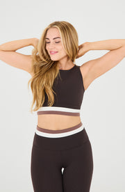 Woman posing with both hands behind her head while wearing the Elastique Athletics Le Monde Bra in dark brown with matching leggings.