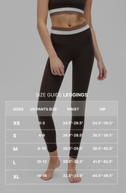 Full body portrait of a woman wearing the Elastique Athletics Le Monde black sleeveless crop top and leggings with size guide.