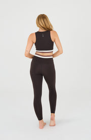 Back view of a woman wearing the Elastique Athletics Le Monde black crop top and leggings set in a minimalist studio setting.