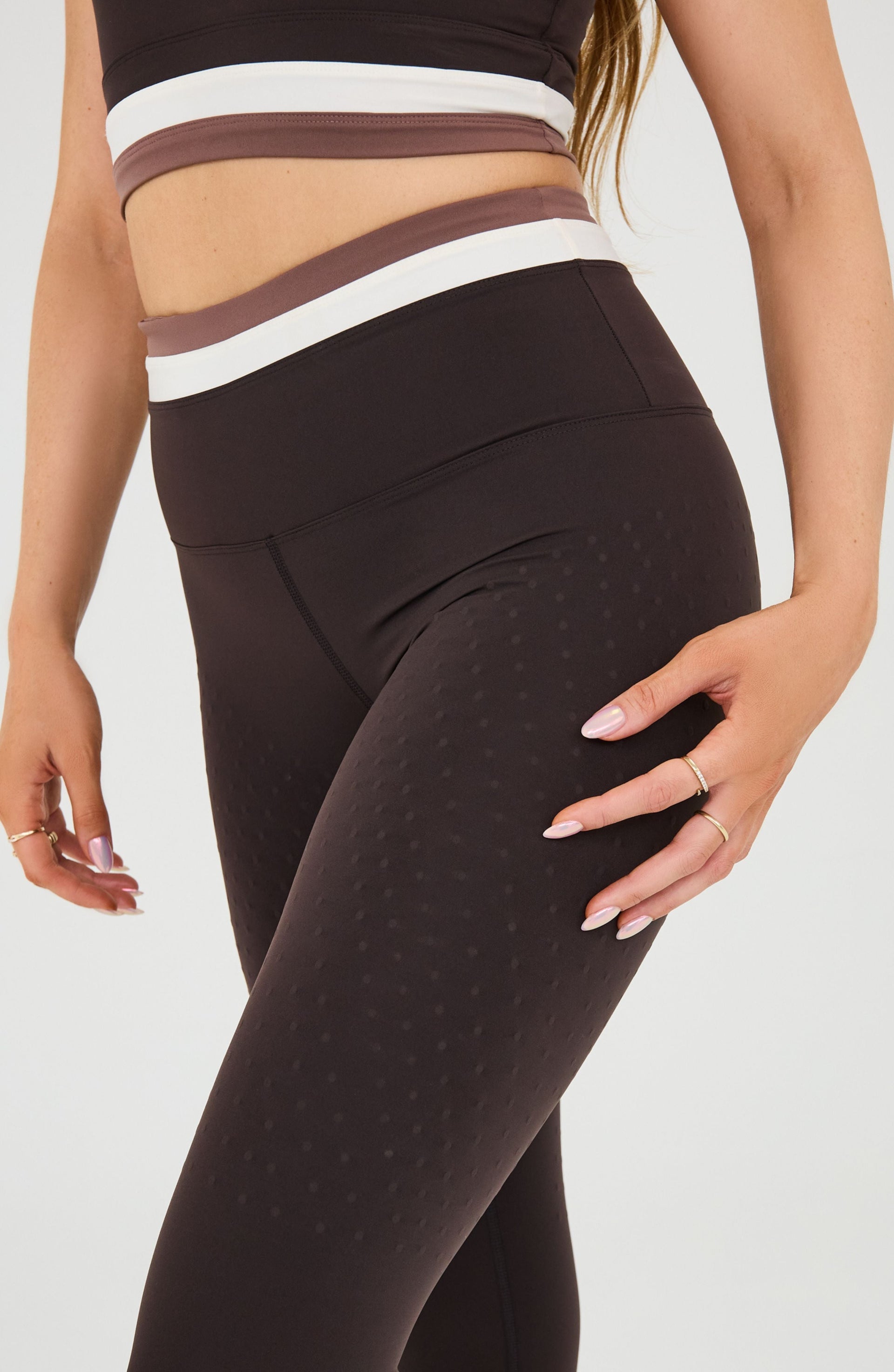 Close up of a woman’s hand resting on the thigh of the Elastique Athletics Le Monde black leggings.