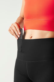 Close up waistband detail of the Elastique Athletics Adorn Leggings in black paired with a bright orange crop top.