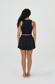 Back view of a woman wearing the Elastique Athletics L'Original Flowy Short in black with a matching sleeveless athletic top.