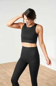 Woman posing in soft shadow lighting while wearing the Elastique Athletics The Fierce Leggings in black with a matching crop top.