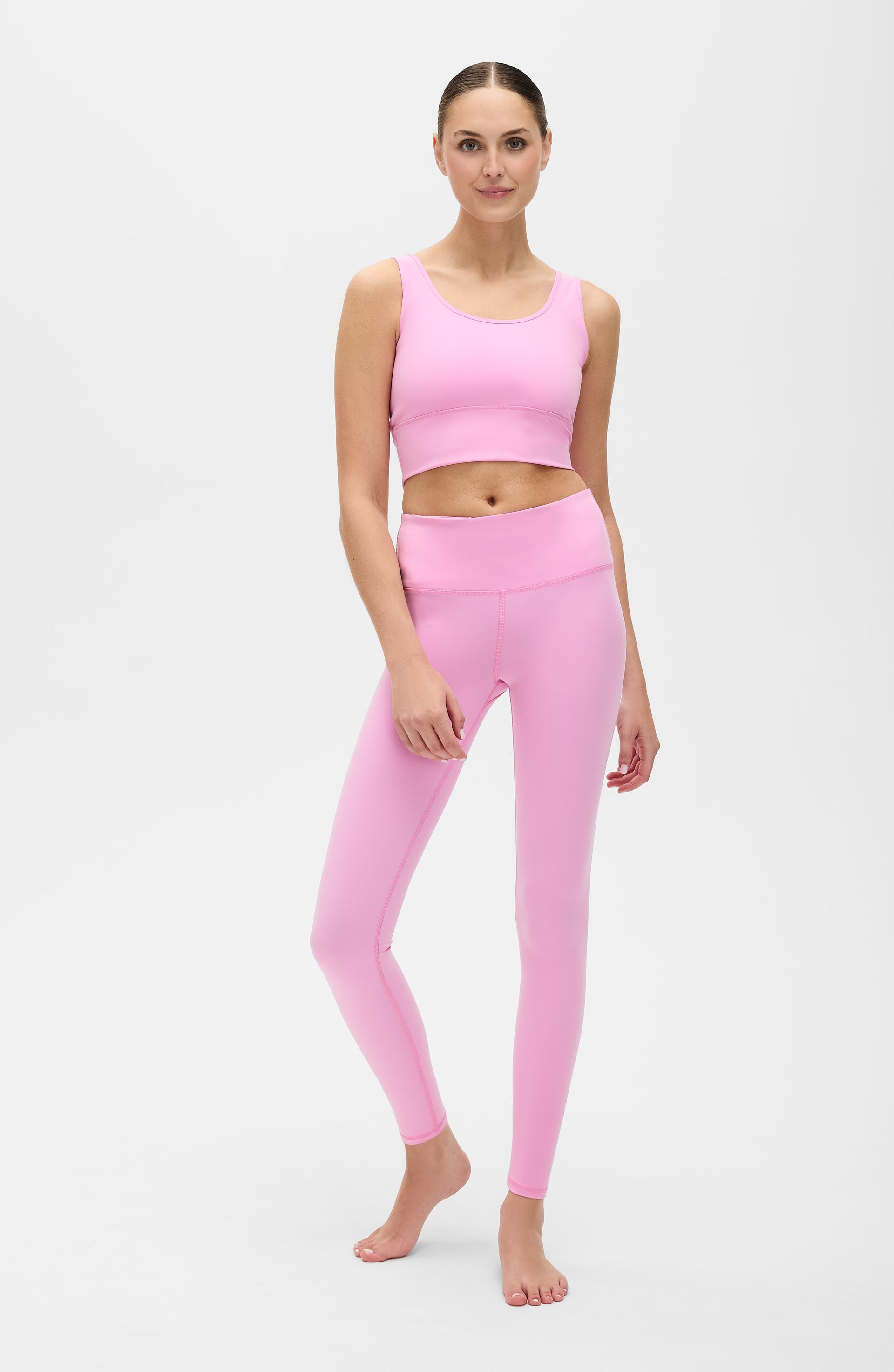 Full body studio portrait of a woman wearing the Elastique Athletics Rise Leggings Vie en Rose in soft pink with a matching sports bra.