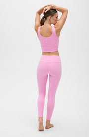 Back view of a woman posing with both arms raised while wearing the Elastique Athletics Rise Leggings Vie en Rose in soft pink with a matching sports bra.