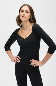 Full body studio portrait of a woman wearing the Elastique Athletics Iconic Sleeve MicroPerle Top in black with matching leggings.
