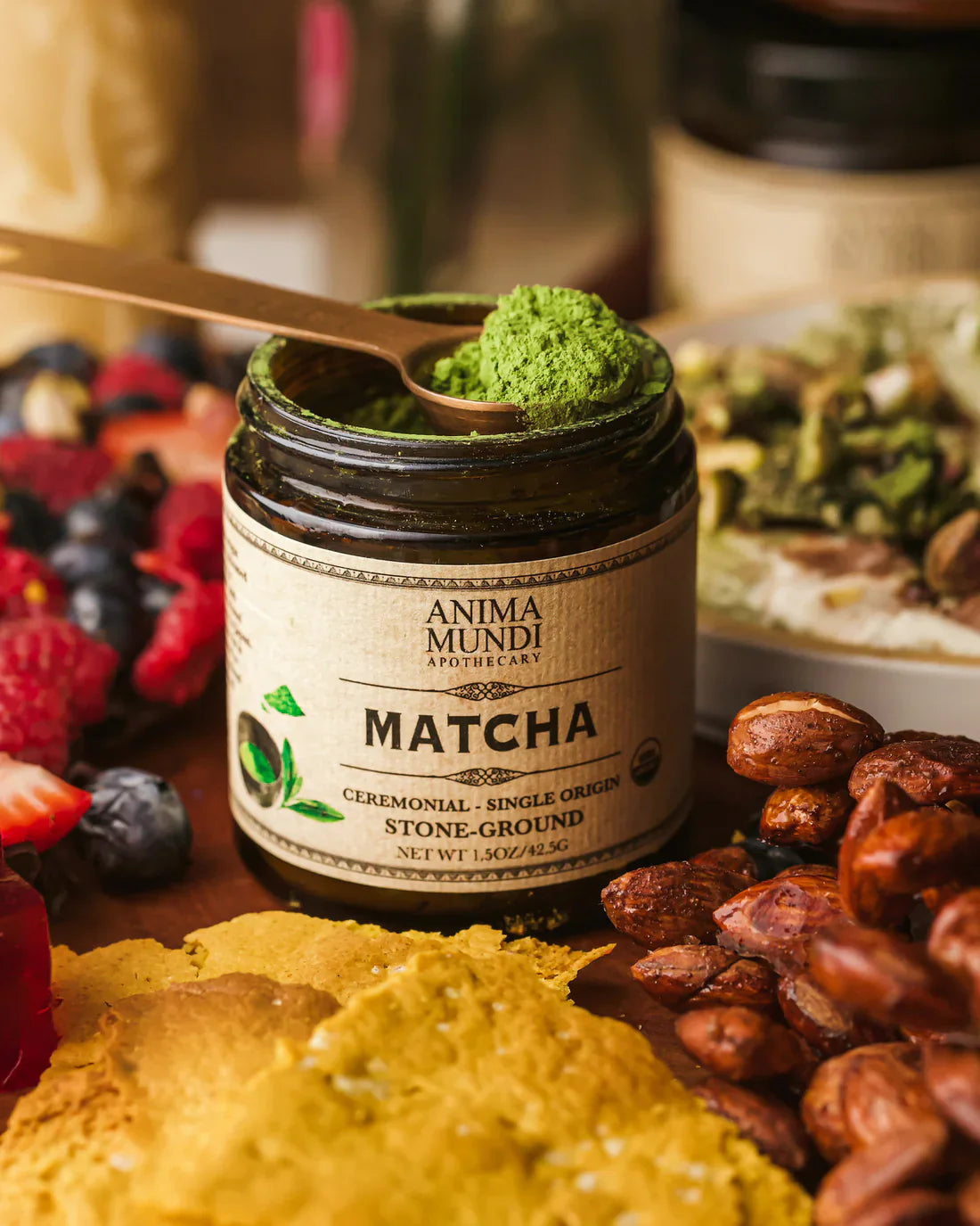 Matcha powder in a wooden spoon beside fresh berries, nuts, and Anima Mundi ceremonial grade matcha.