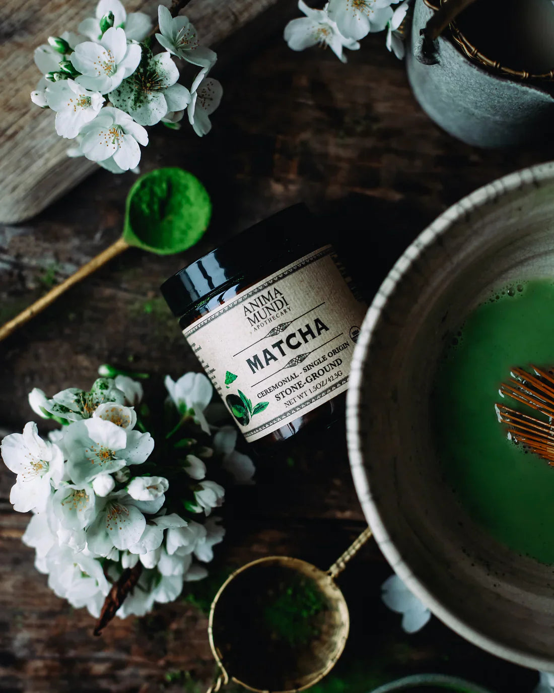 Anima Mundi ceremonial grade matcha beside a traditional whisk and bowl with blooming white flowers.