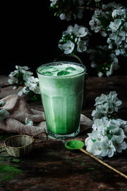 Iced matcha latte garnished with white blossoms and vibrant green matcha powder on a rustic tabletop.