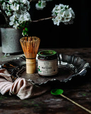 Traditional bamboo matcha whisk displayed with Anima Mundi Matcha and tea preparation tools in warm natural light.