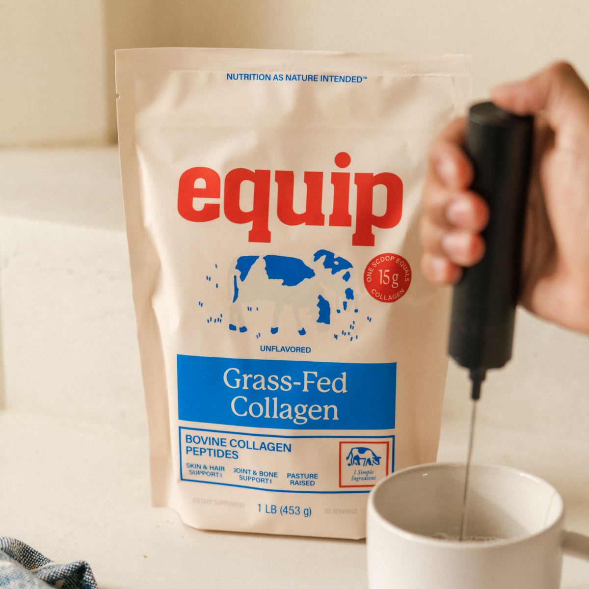 Equip Grass-Fed Collagen unflavored pouch beside a white mug as a handheld frother mixes the drink.