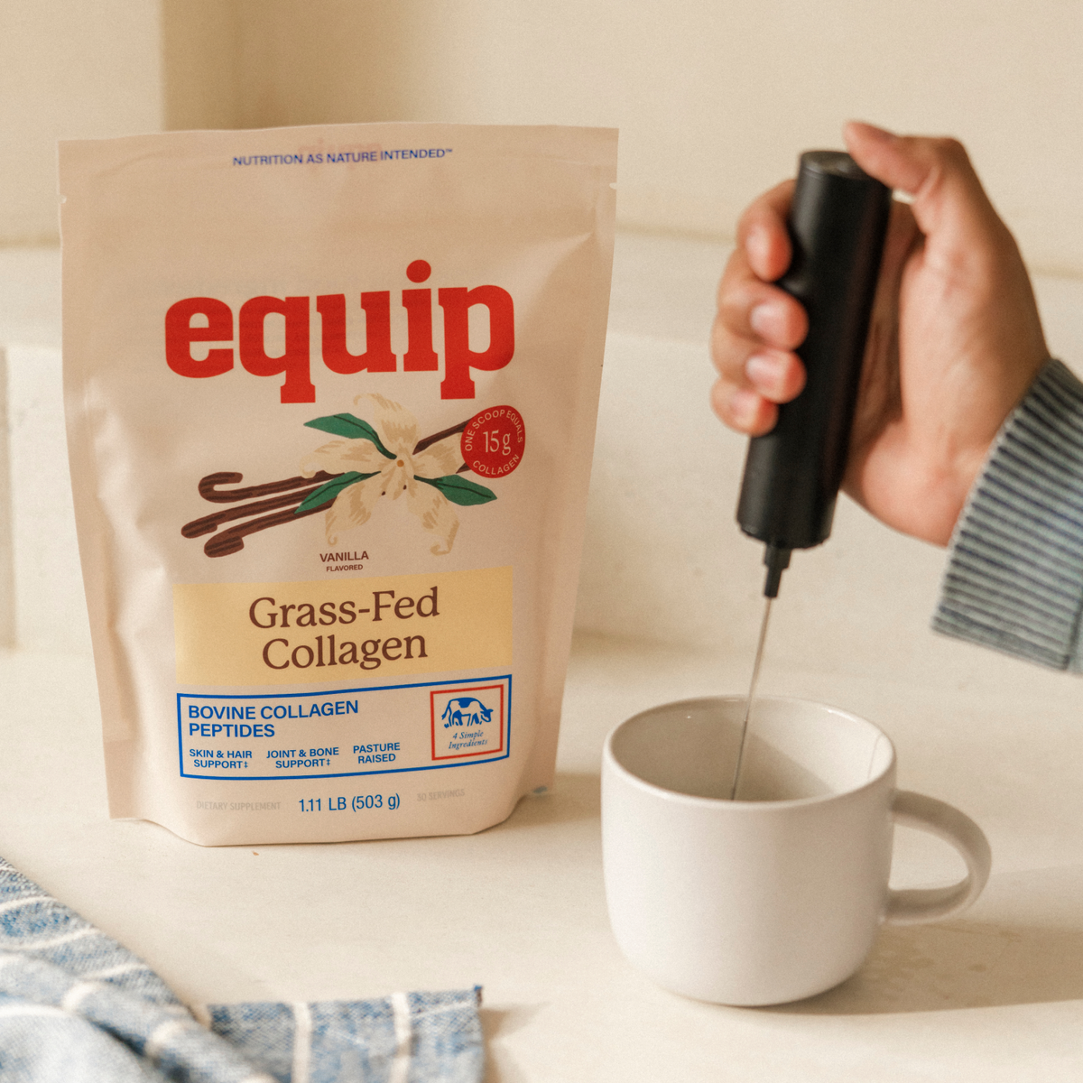 Equip Grass-Fed Collagen vanilla pouch beside a white mug as a handheld frother mixes the drink.