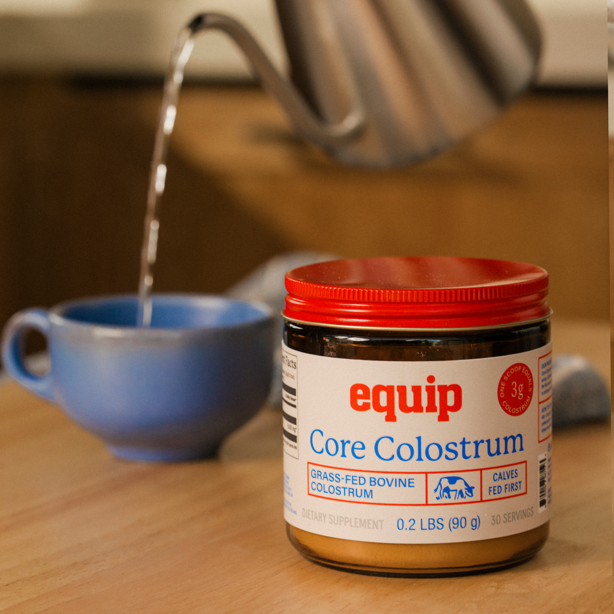 Equip Core Colostrum jar beside a blue cup as hot water is poured from a kettle.