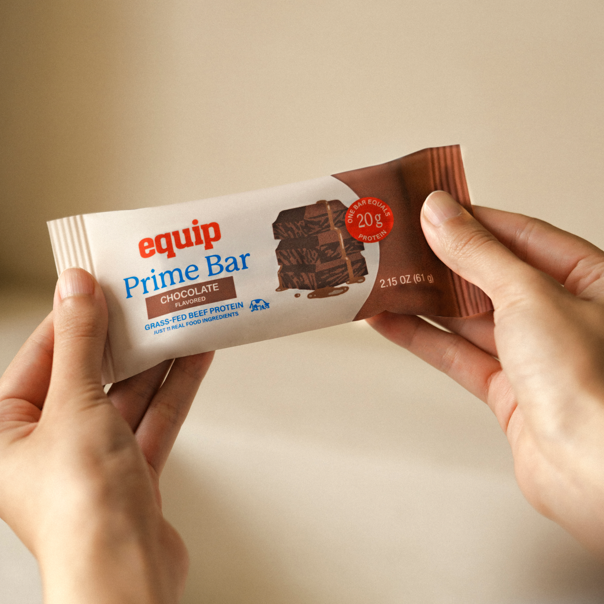 Equip Prime Bar chocolate protein bar in wrapper held beside a broken chocolate bar