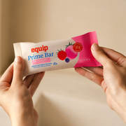 Equip Prime Bar mixed berry protein bar in pink wrapper held in one hand