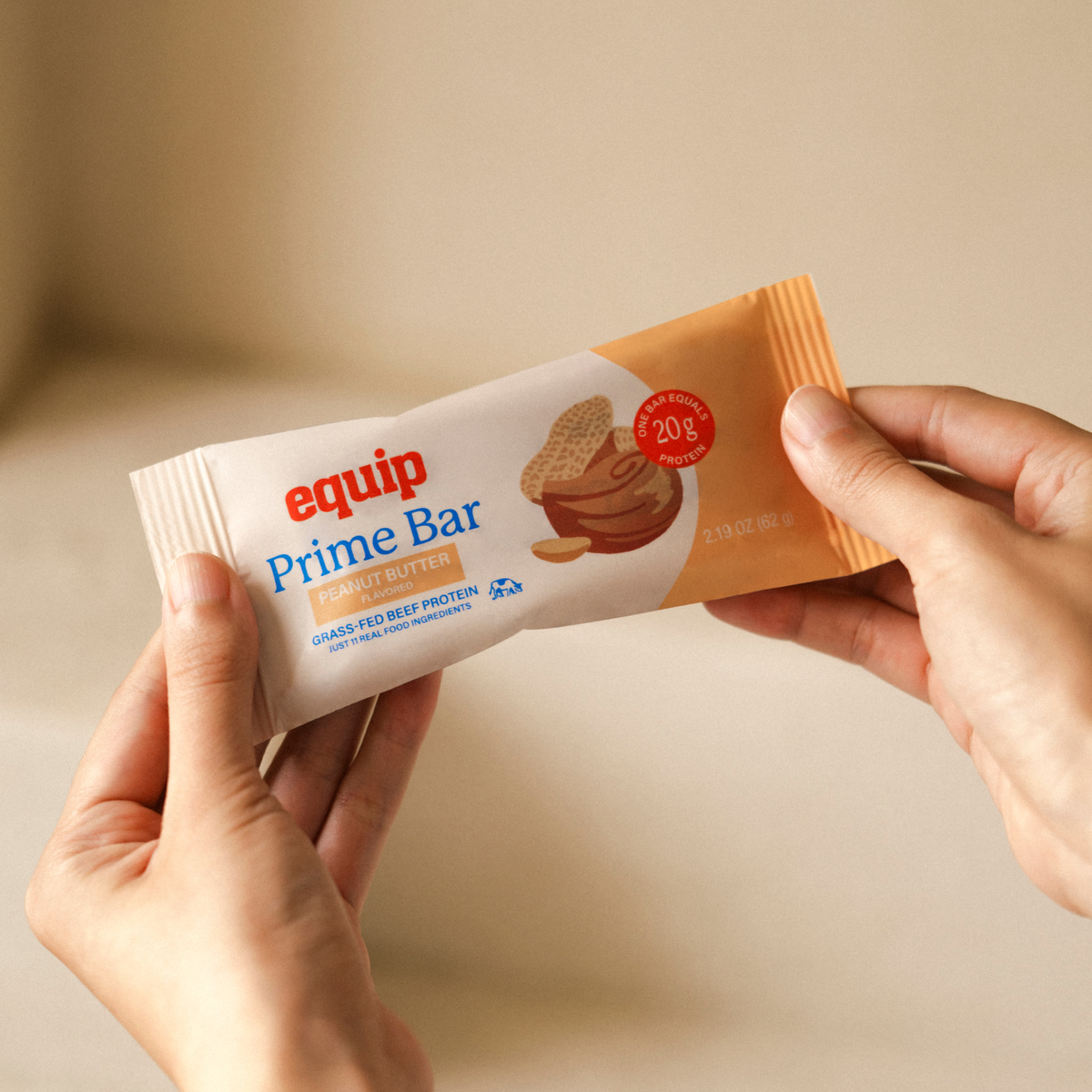 Equip Prime Bar peanut butter protein bar in orange wrapper held in one hand