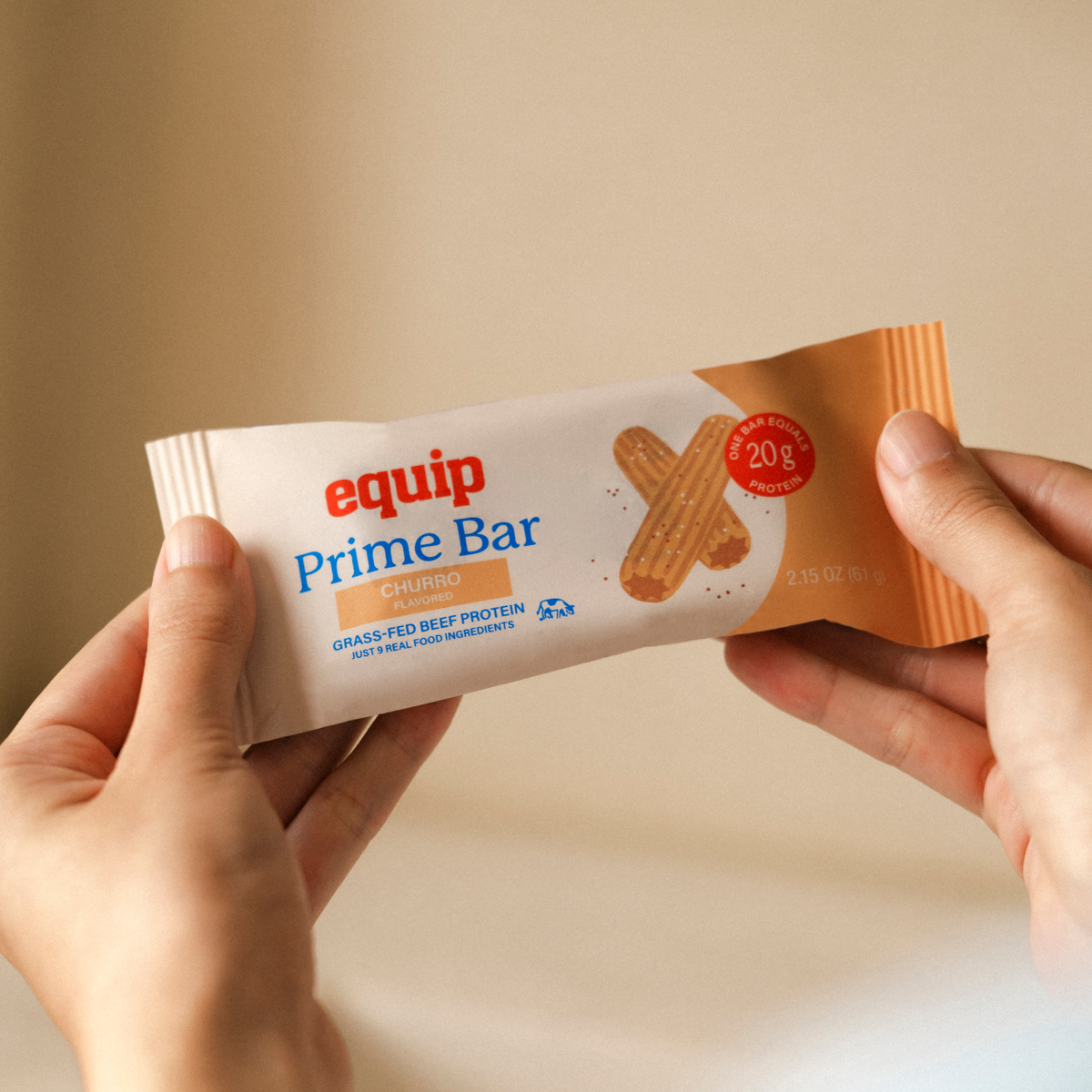 Equip Prime Bar churro protein bar in orange wrapper held in one hand