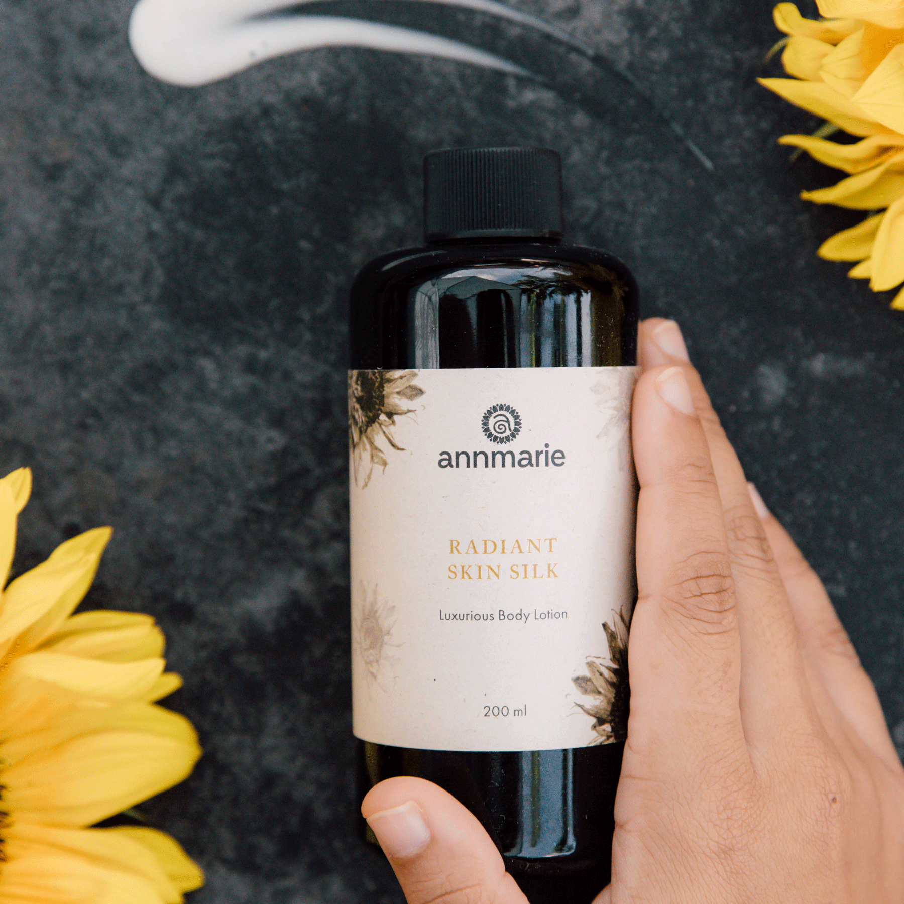 Annmarie Radiant Skin Silk Body Lotion displayed with botanical elements and sunflower accents