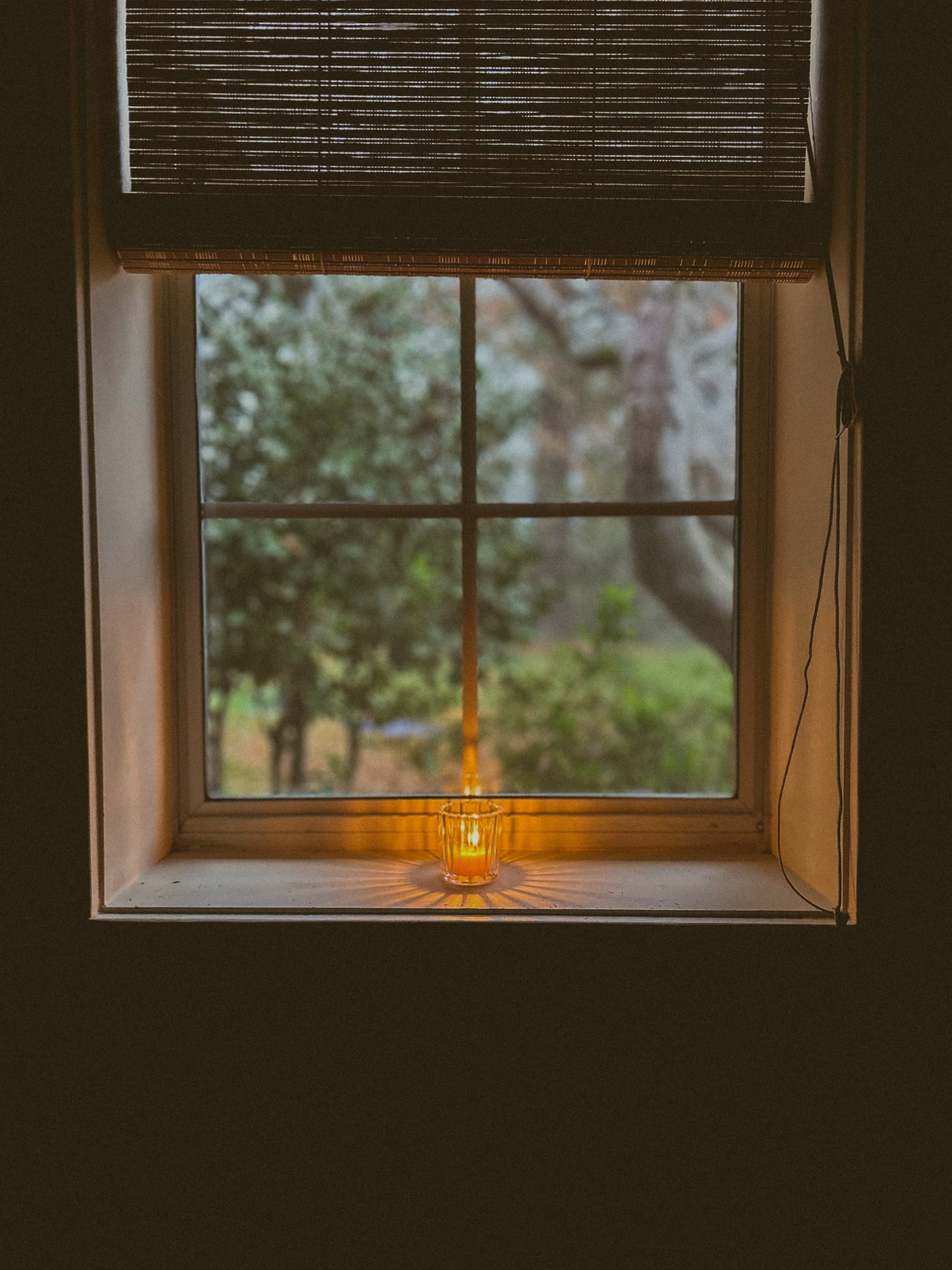 Lit Busy Bees Ribbed Glass Tea Light Holder glowing on a windowsill in a dimly lit room.