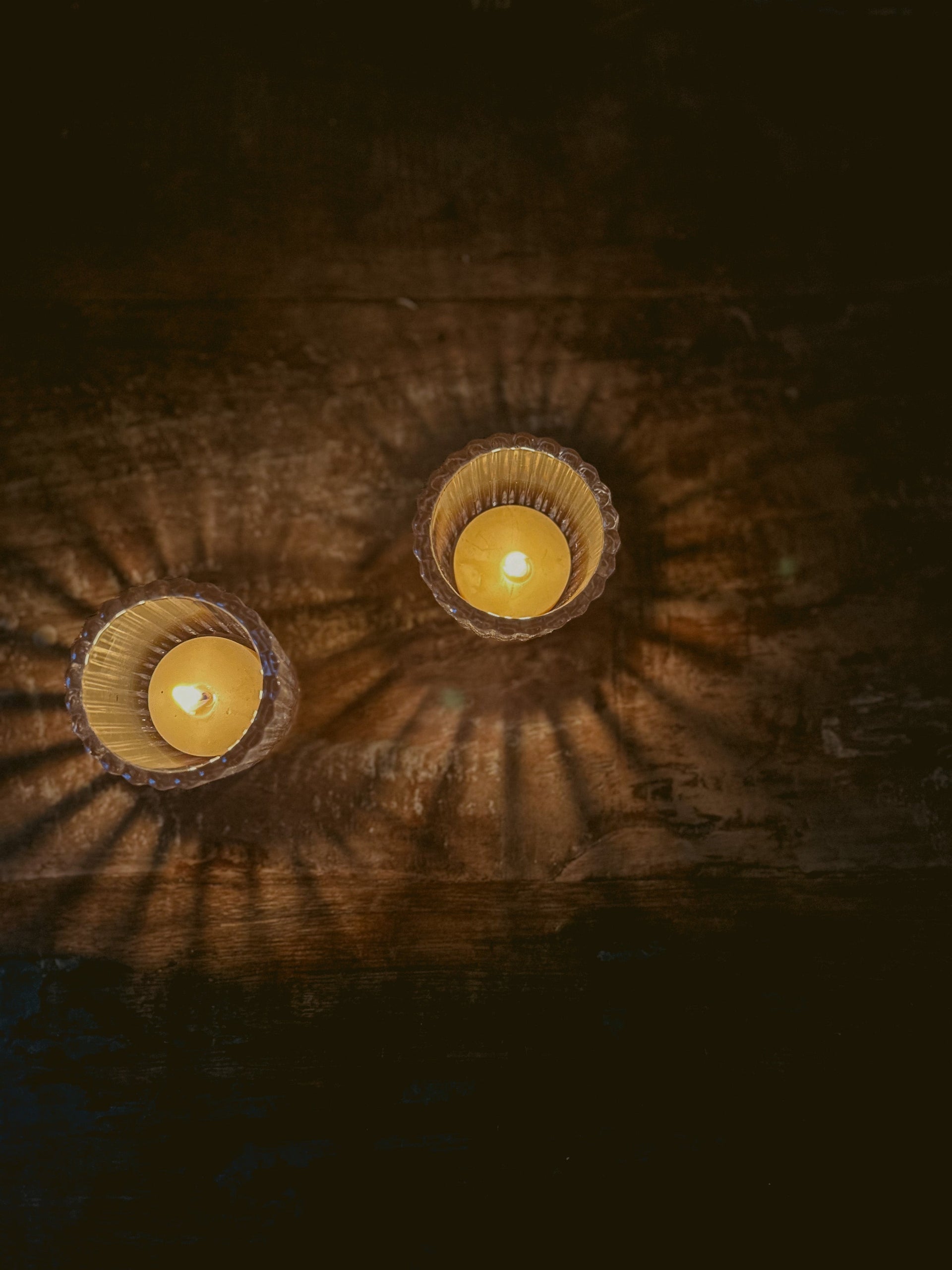Overhead view of lit Busy Bees Ribbed Glass Tea Light Holders creating circular light reflections in a dark room.