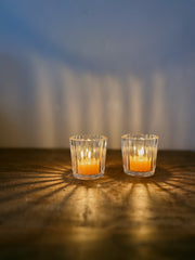 Busy Bees Ribbed Glass Tea Light Holder with lit candles casting warm patterned shadows across a wooden surface.