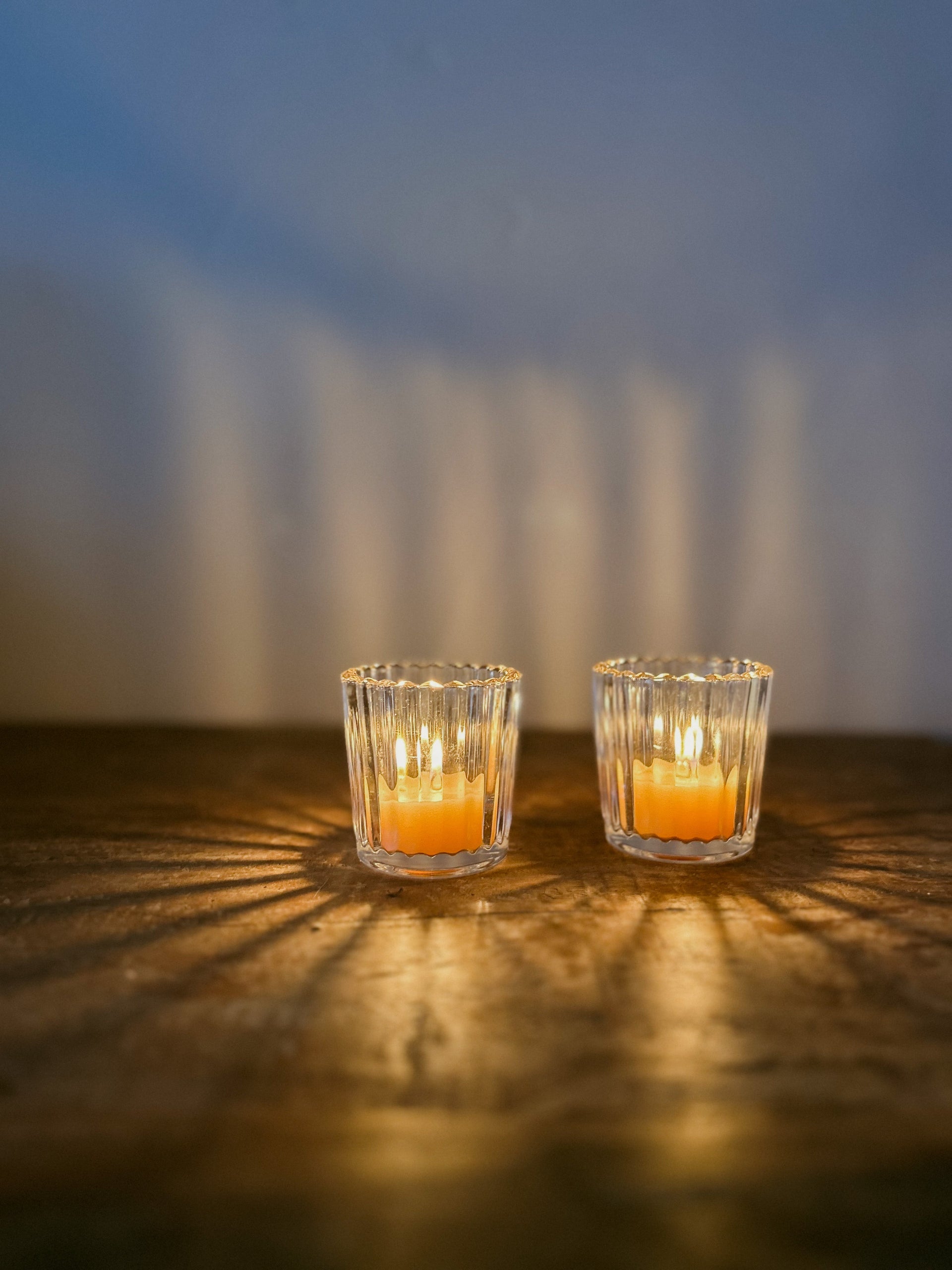 Busy Bees Ribbed Glass Tea Light Holder with lit candles casting warm patterned shadows across a wooden surface.