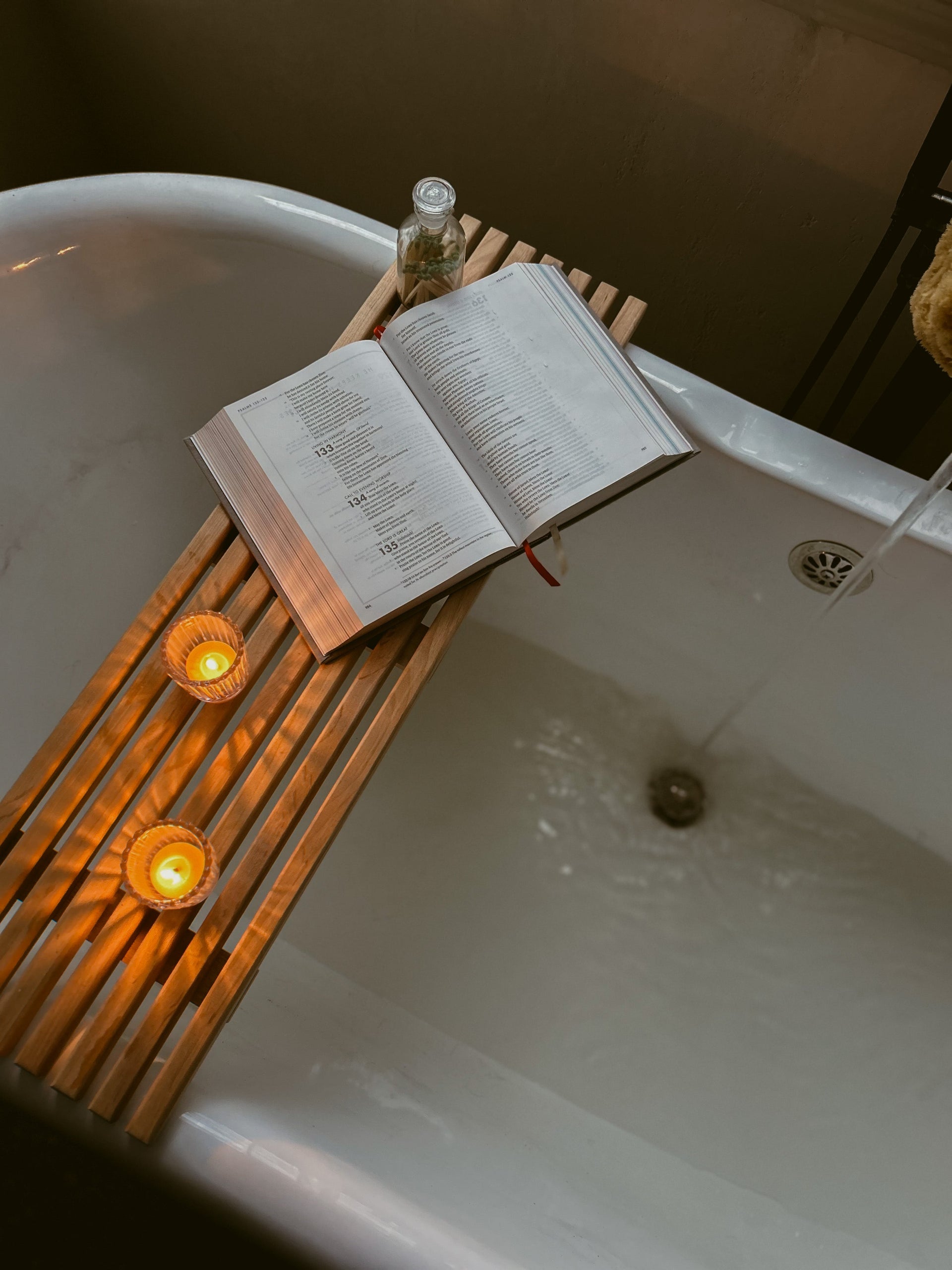 Open book resting beside lit Busy Bees Ribbed Glass Tea Light Holders in a cozy bath setting.