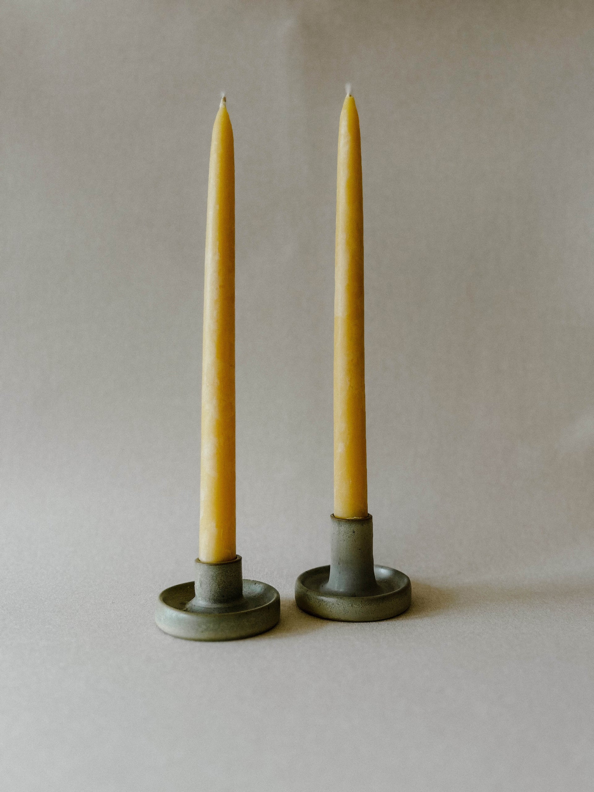 Two lit Busy Bees Hand Dipped 9 Inch Taper Candles displayed in brass holders against a neutral background.
