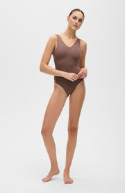 Full body studio portrait of a woman wearing the Elastique Athletics Adorn taupe sleeveless bodysuit.